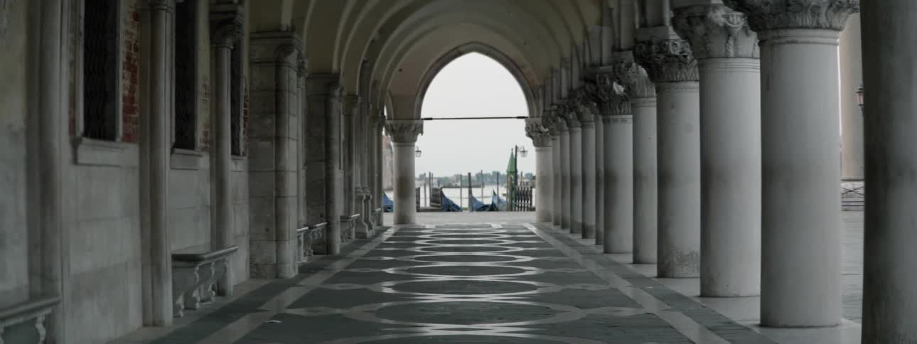 A walkway with an arch and columns leading out to a body of water