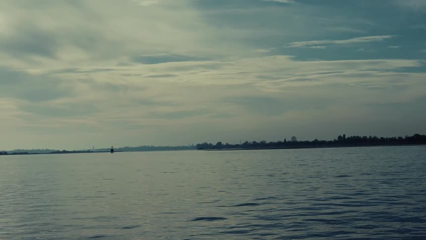 A serene wide shot of still water beneath a cloudy sky with a distant treelined shore