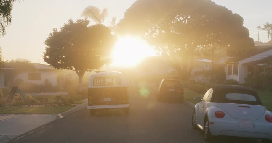 A vintage vw van drives through a quiet suburb at sunrise evoking nostalgia and calm