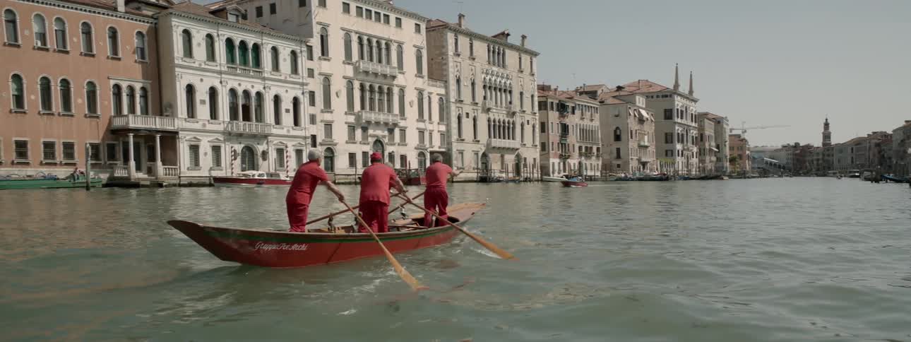 Four men are rowing a boat in a canal in venice, italy