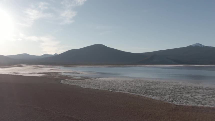 A beach with still water and mountains in the background