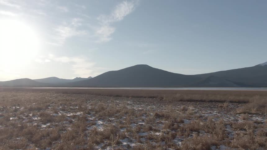 A wide sunlit view of dry grasslands stretching out toward a distant mountain range under a clear sky
