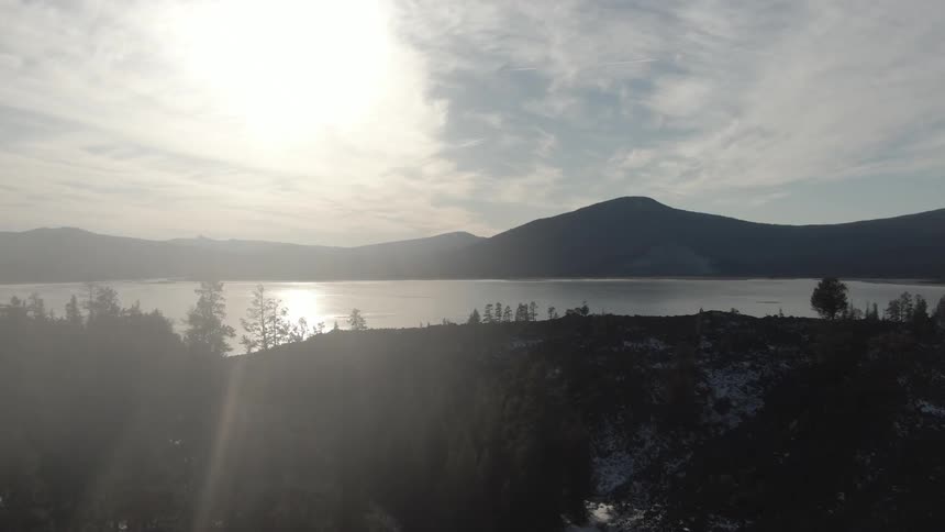 A road cutting through a fir forest leading to a large lake with mountains in the distance