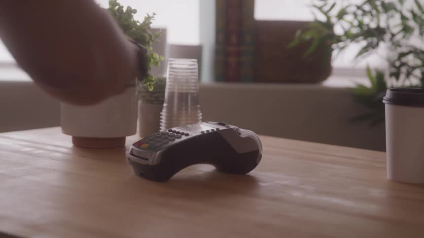 A person tapping a smartwatch on a credit card machine to buy an isolated coffee cup
