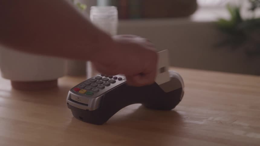 A person swiping a credit card on a card machine placed on a table