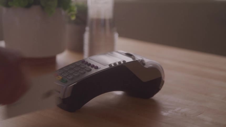 A person swiping a credit card on a card reader to purchase a coffee cup