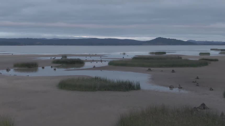 A view of a beach is shown with hills rolling in the background