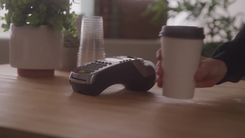 A person pays by card and picks up a coffee in a cozy cafe