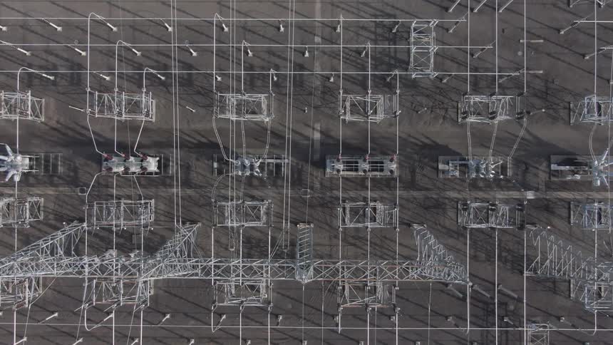 Aerial shot of an electrical substation with metal frameworks and shadow patterns on the ground
