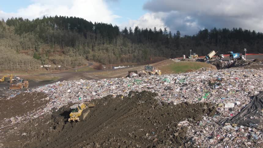 Aerial shot of tractors clearing an open ansel dump with a forest in the background