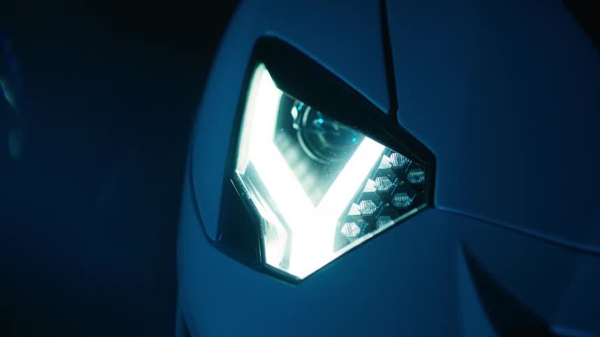 A cars headlight blinks brightly in a dramatic closeup shot with a cool blue tint