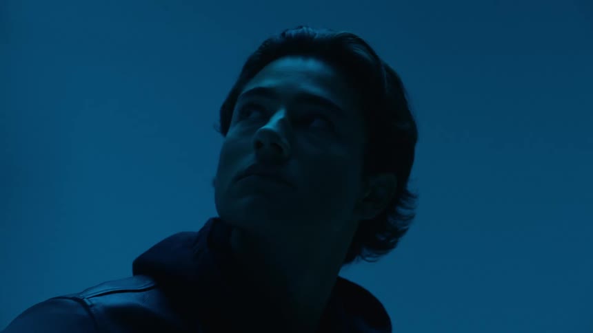 Man leaning against a parked car in an area lit by blue lighting looks around