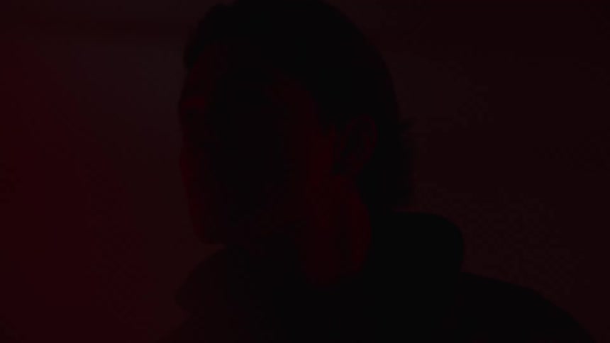 A person with mediumlength hair is illuminated by blue and red lighting against a blue background