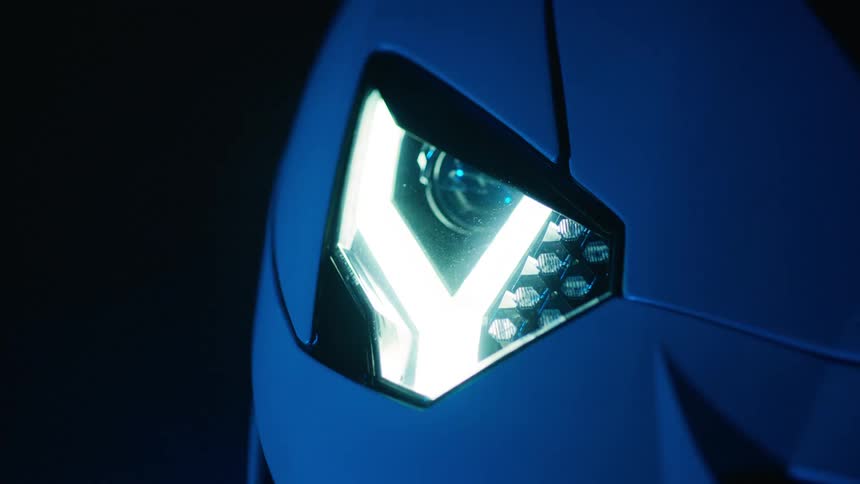 A closeup of a futuristic car headlight shifting from blue to red in a dark setting