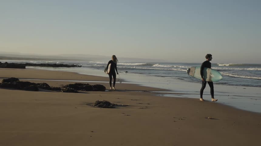 Two surfers are walking on the beach while carrying surfboards