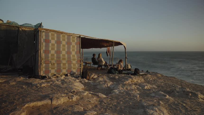 Three people sitting in a tent by the sea