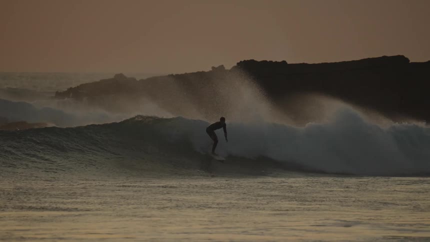 Surfer riding intense fast rolling wave at sunrise