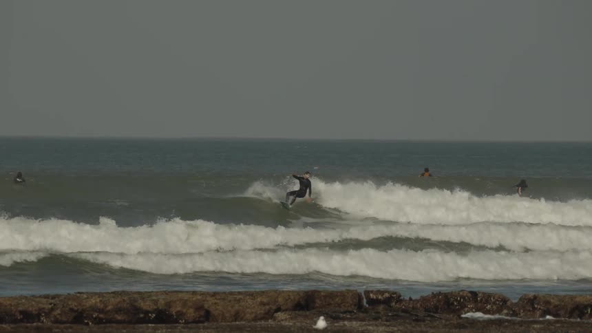 A group of people are surfing near a rocky shore on a cloudy day