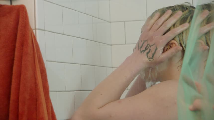 Blonde woman showers in a white tiled shower