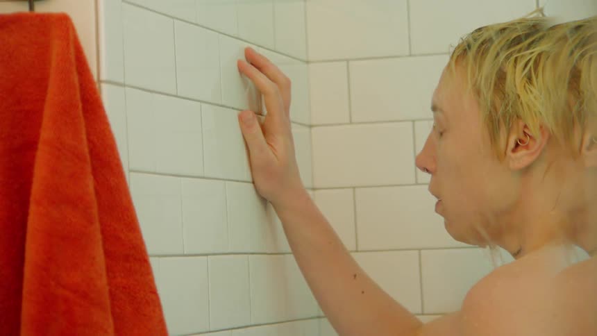 Blonde woman takes a shower in a white tiled shower