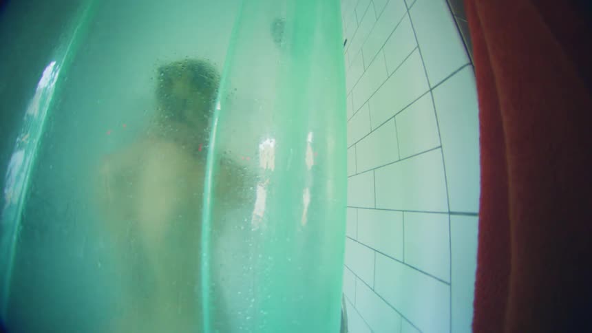 A man taking a bath in a bathroom dancing seen through the blurred bathroom glass at midday
