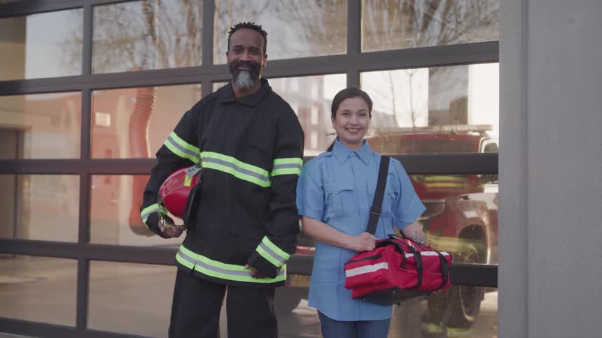 Emergency services personnel pose next to a fire station during the daytime