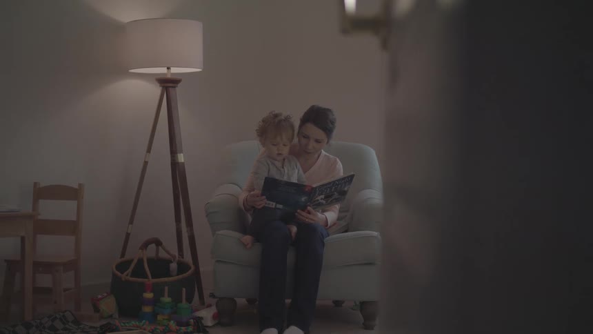 Mother sitting in an armchair reading a book with her little son
