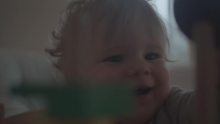 At midday a baby laughs with excitement while playing with toys