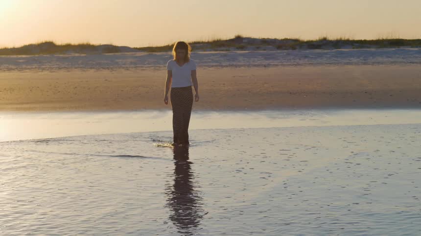 A woman wearing a long skirt walks into the water at a beach