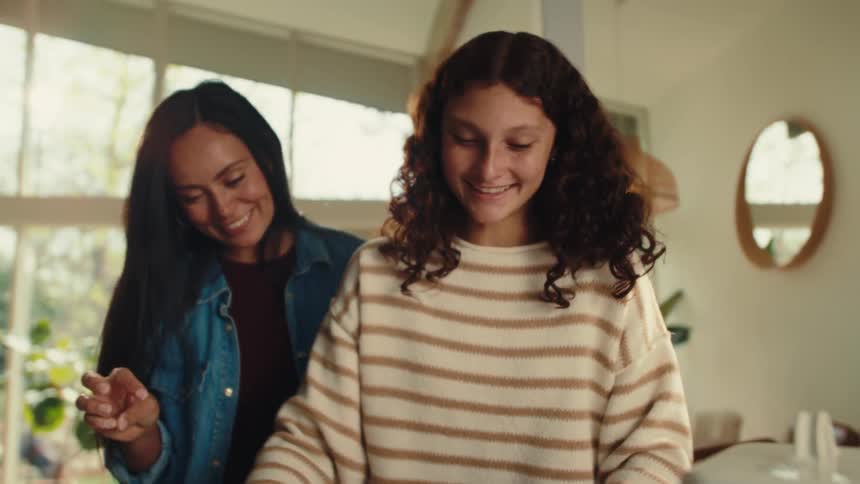 A mother and daughter are using a rolling pin on dough in the kitchen