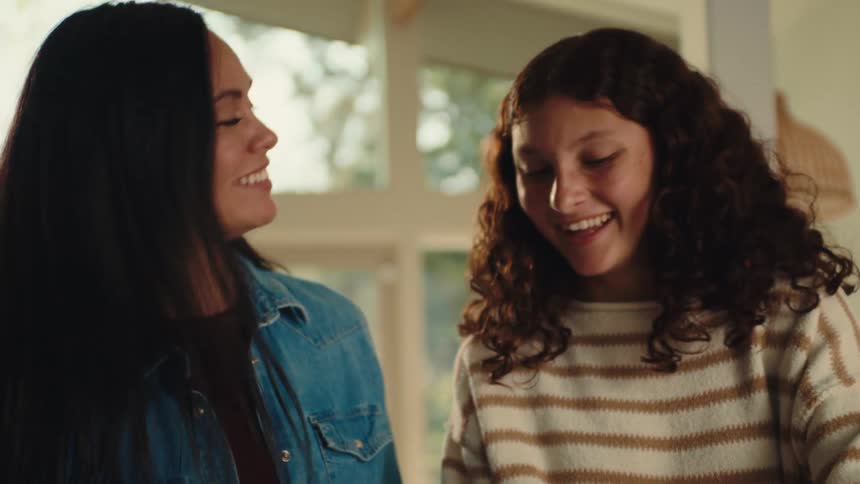 A woman and a teenage girl are using cookie cutters to shape dough on a lightcolored countertop