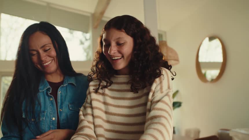 A woman and a teenager are happily making cookies together in a bright room