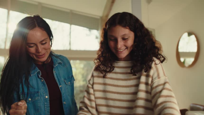 A mother and daughter joyfully roll out dough together on a kitchen counter sharing a fun and bonding moment