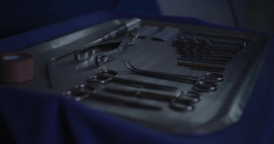A persons hand taking a blue cloth off a metal tray with various cutting tools