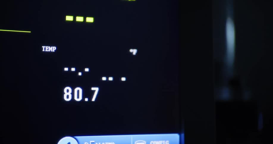 A digital medical monitor displays a patients body temperature in a dimly lit hospital or clinical setting