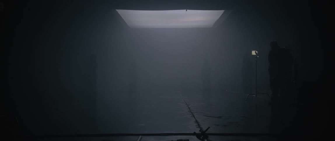 A film set is enveloped in white mist fog or smoke with lighting equipment a track and cloaked figures in the background