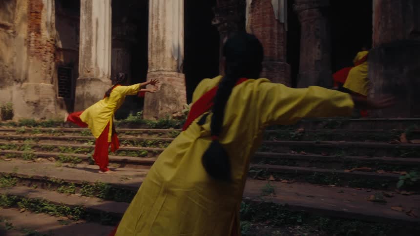 Members of a female dance troupe wear matching outfits while dancing at a ruined landmark building