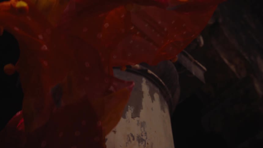 Bright colorful fabrics dramatically flows in slow motion near a metal object in a dark industrial setting