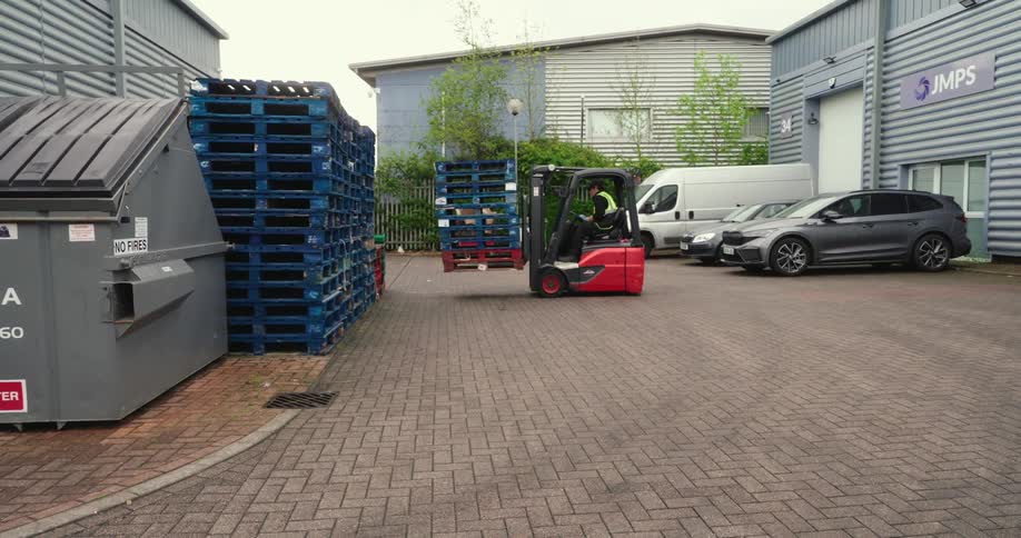 A person driving a forklift carrying some blue pallets out of a stack