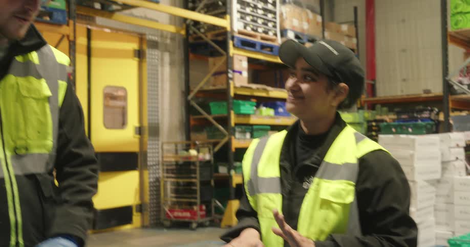 Three warehouse workers in highvisibility gear share a cheerful moment while conversing inside a storage area