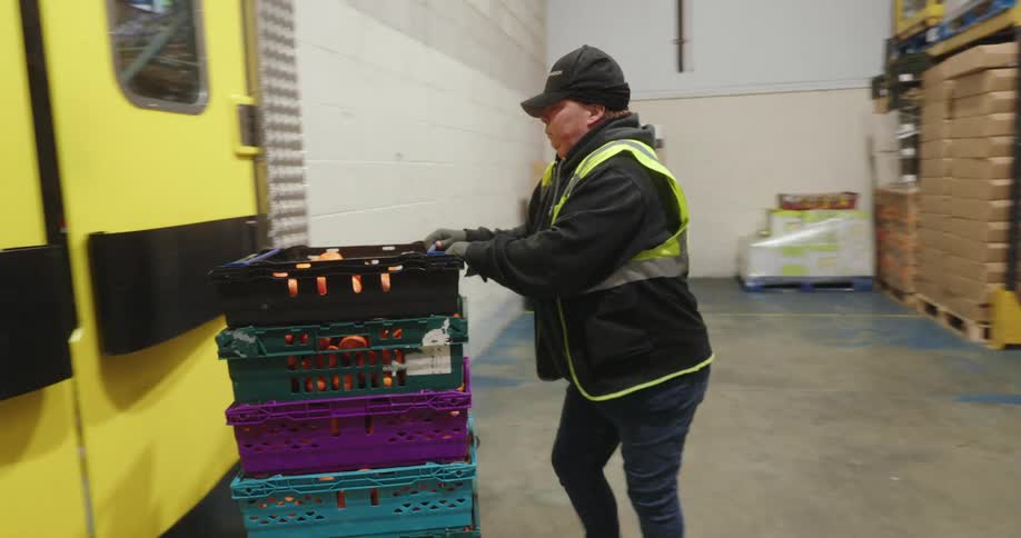 A person wearing a highvisibility vest and a cap pushes crates through yellow doors in a warehouse
