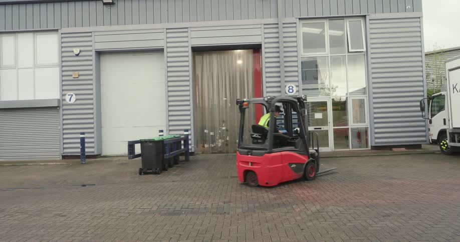 A person wearing a green vest reversing a red forklift