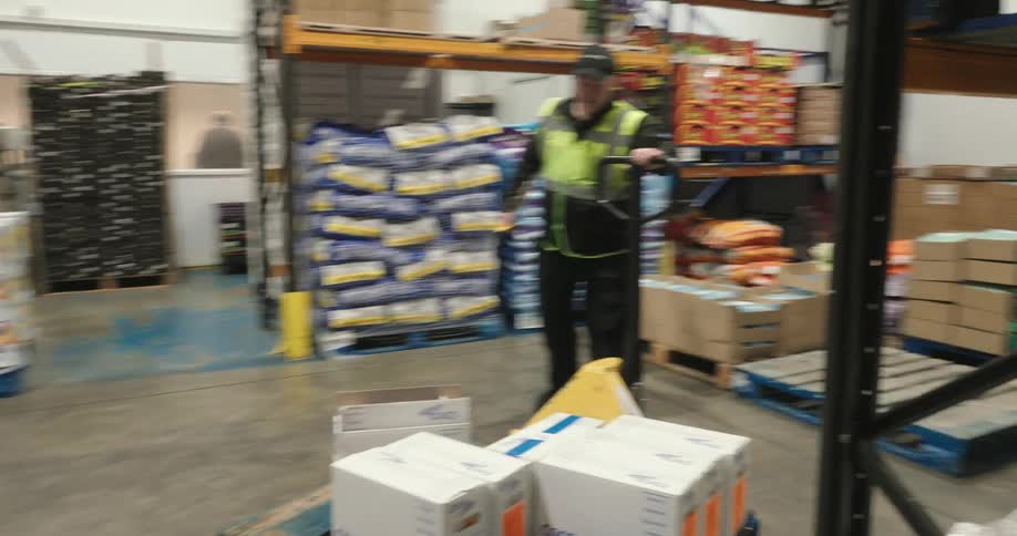 A worker moves boxes in the warehouse with a pallet jack