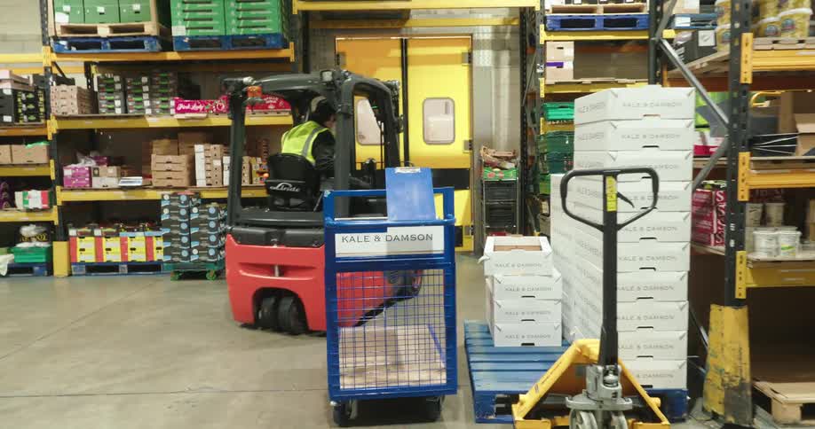 A man in a green vest is driving a forklift and passing through a yellow double door