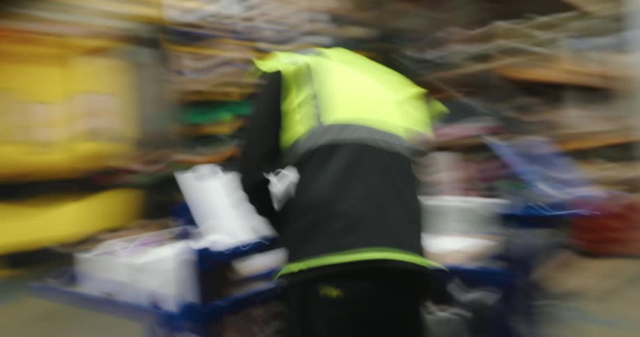 A person wearing a highvisibility vest and a cap pushes a cart through a warehouse