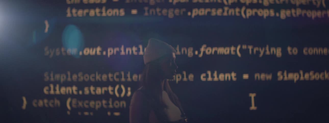A woman is standing in front of a wall with projections of code flashing on it