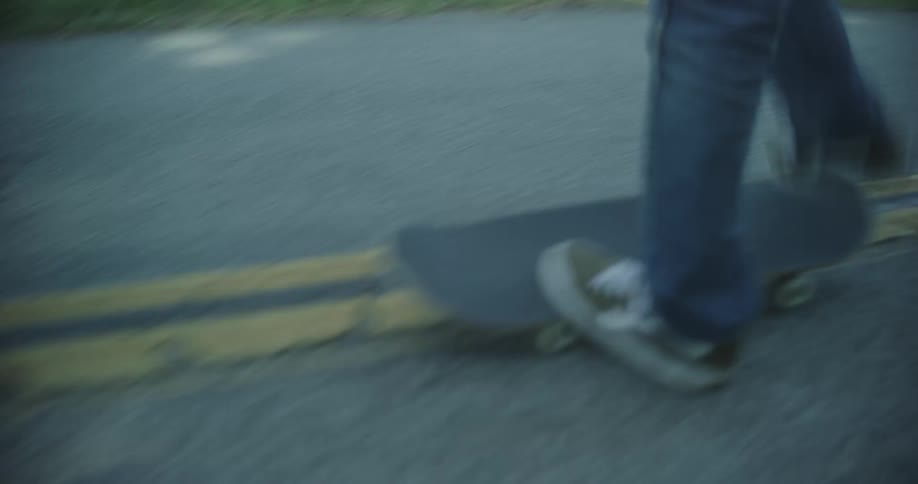 A person skateboards down a road with old camper vans parked on the side before tripping and falling