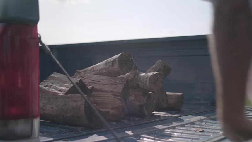A man loads firewood into the back of a truck and closes the tailgate