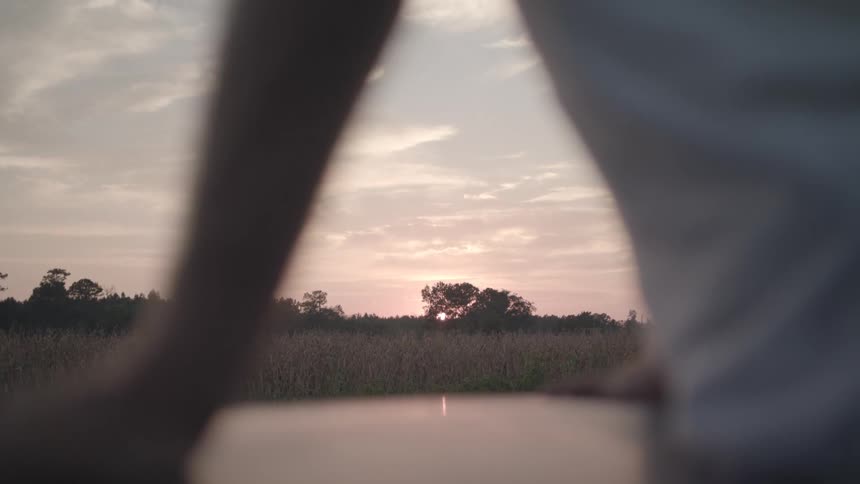 Body of a person sitting in a vehicle overlooking a field and the sunset on the horizon