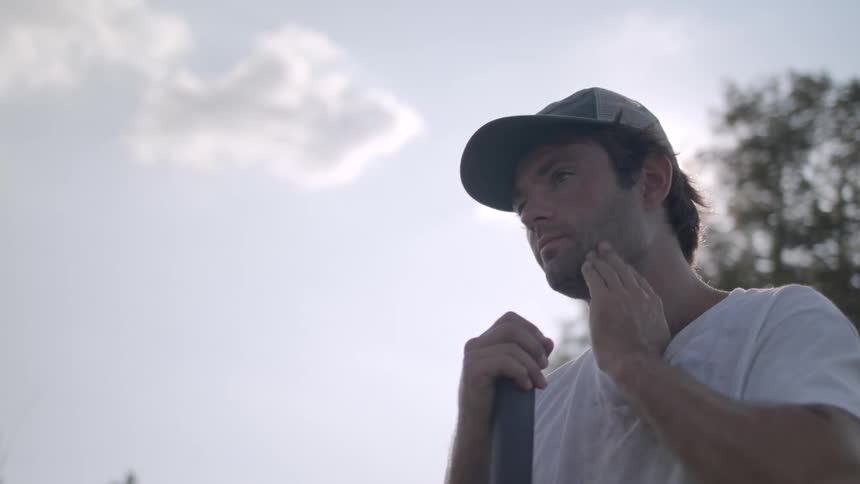 A man leans on a stick and wipes his face